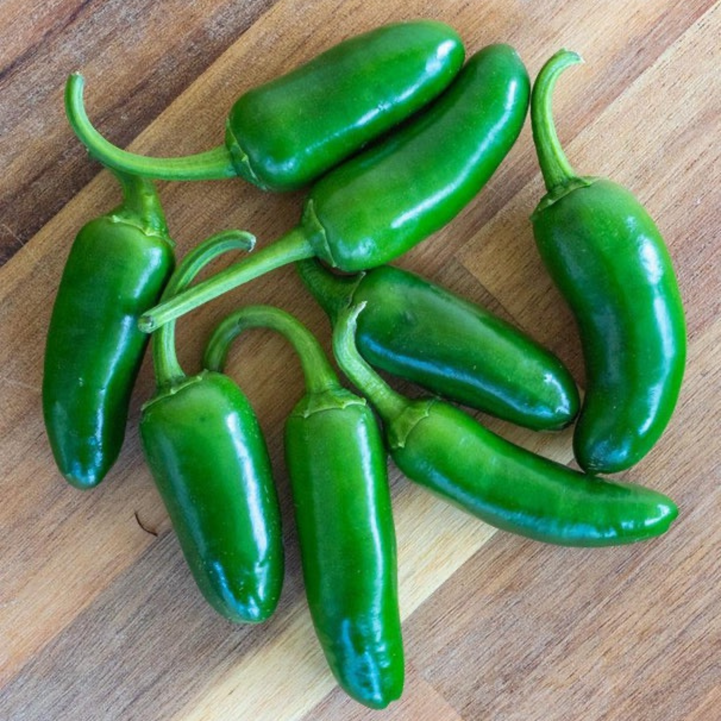 a bunch of bright green jalapeño peppers resting on a wooden surface