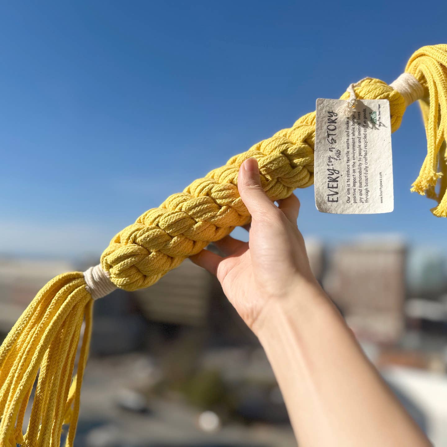 A person holding up a large yellow macrame candy rope designed for big dogs.