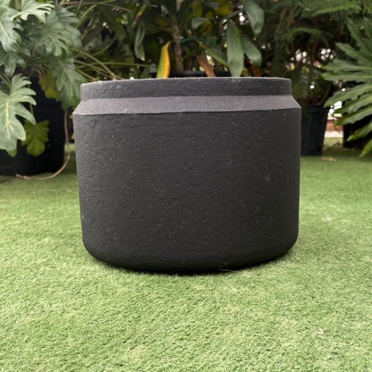 a close up of a small latte round planter resting on a grass like background in a greenhouse setting
