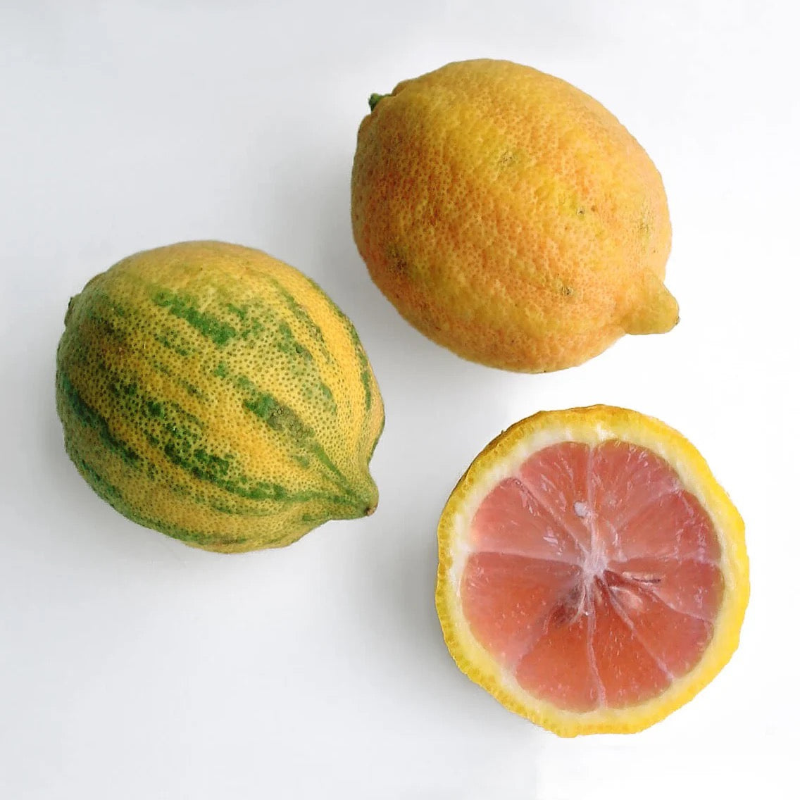 three lemons with one cut open and is pink inside against a white surface
