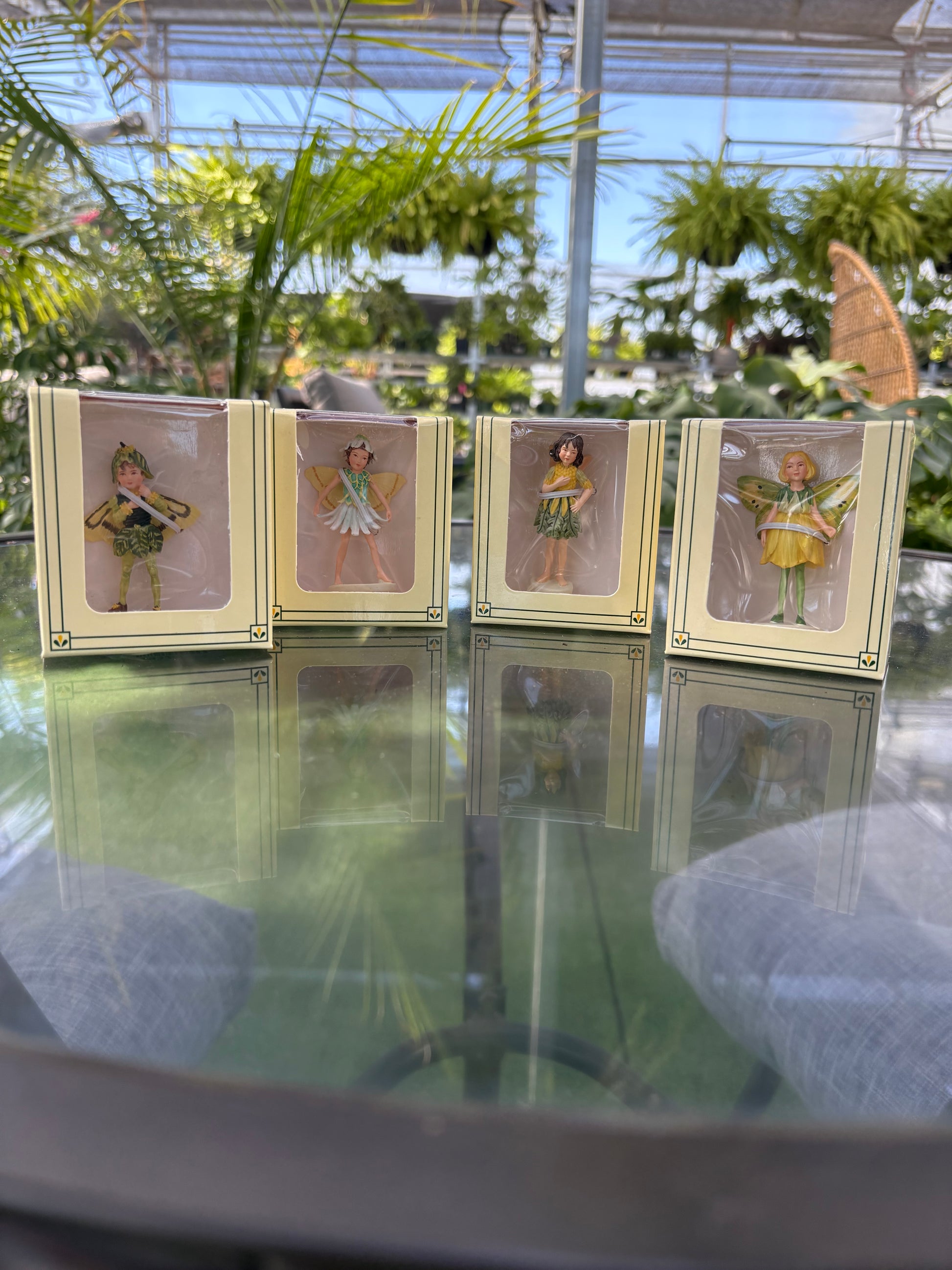 4 packaged mini garden fairies side by side in a greenhouse setting