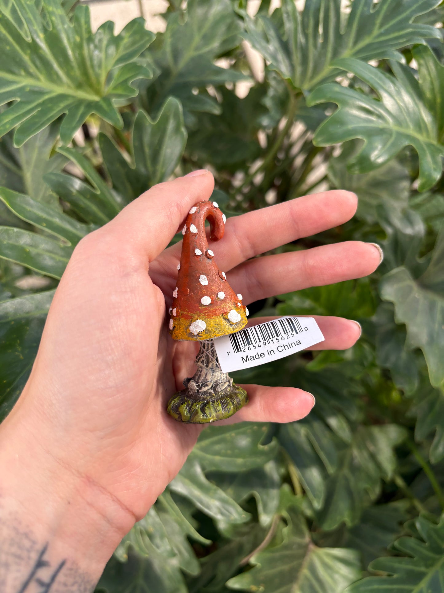 Hand holding a small mini toadstool  with a barcode label against a green leafy background