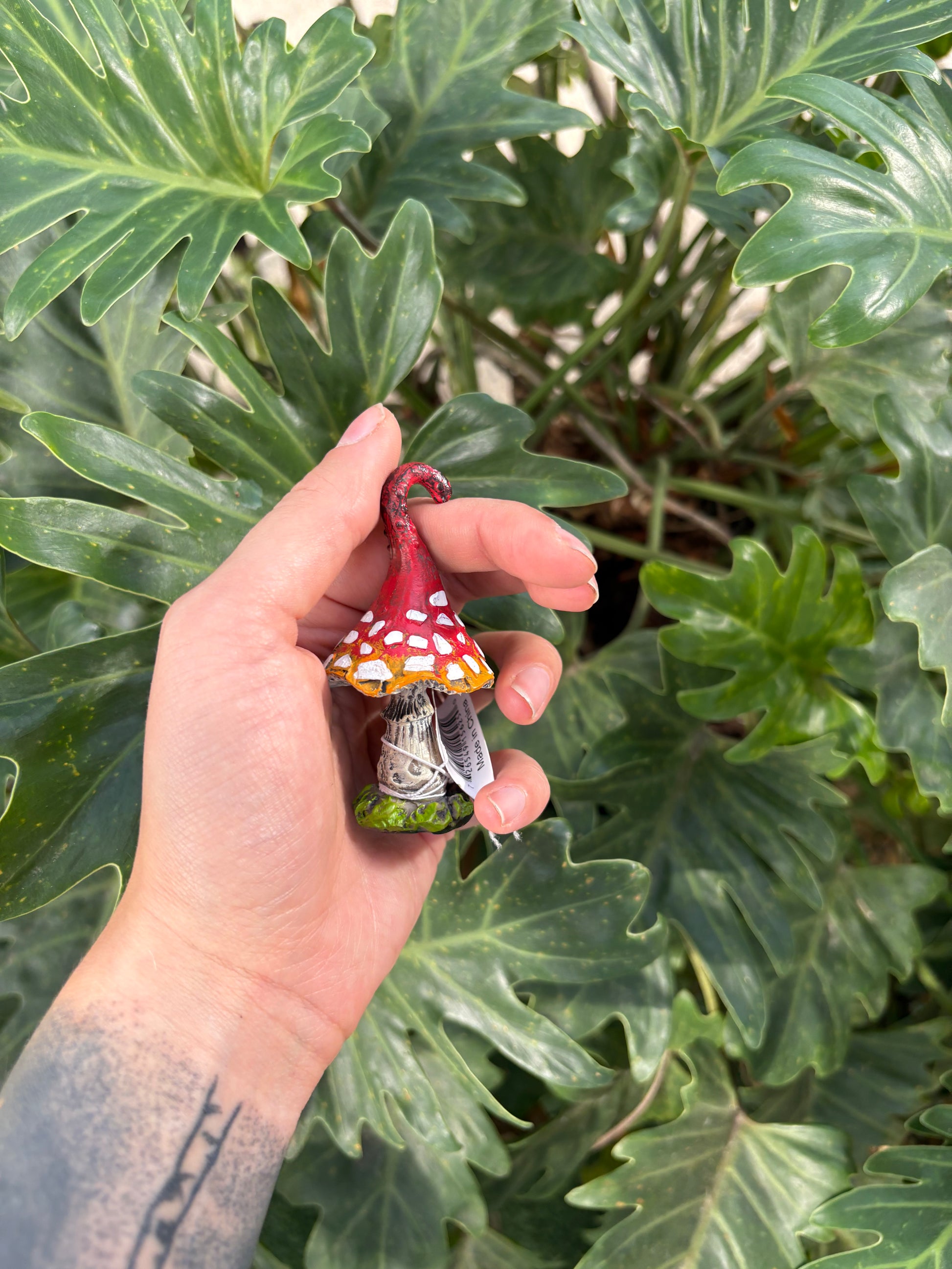 Hand holding a small mushroom figurine in front of green leaves