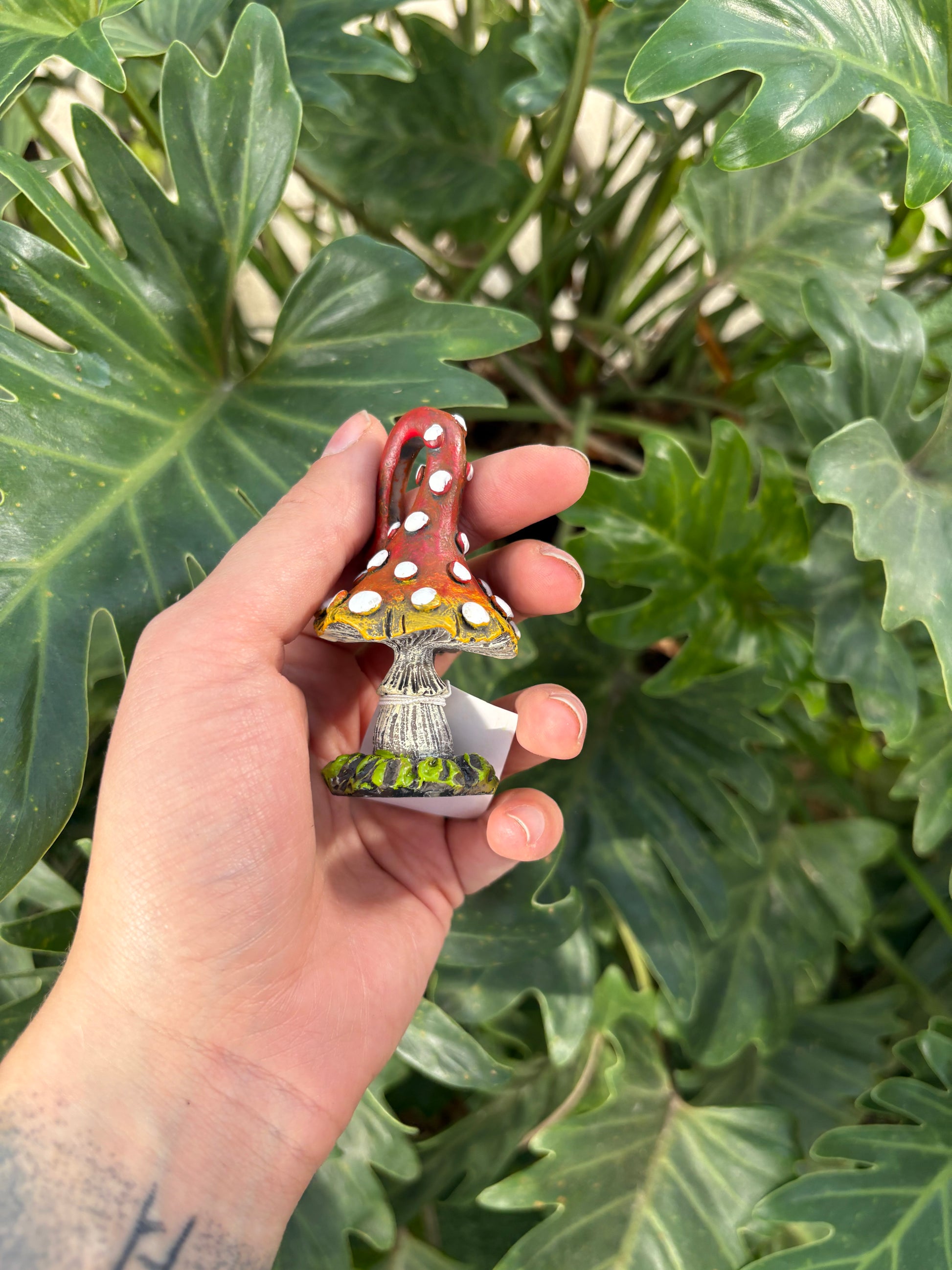 Hand holding a small mini toadstool figurine with a plant in the background
