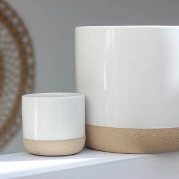 Two modern pots with two toned designs, one large and one small, placed on a surface with a woven object in the background.