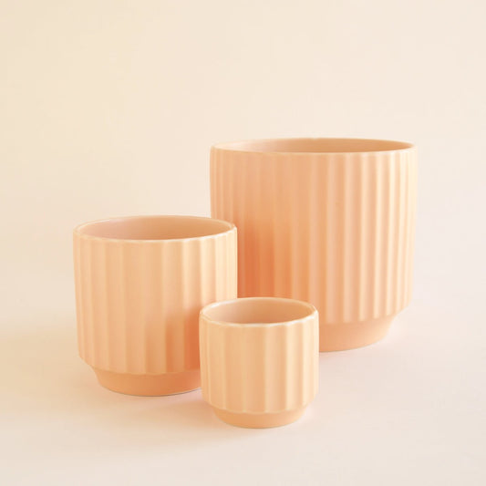 Three peach-colored monroe planter sunset ceramic planters of different sizes on a beige background