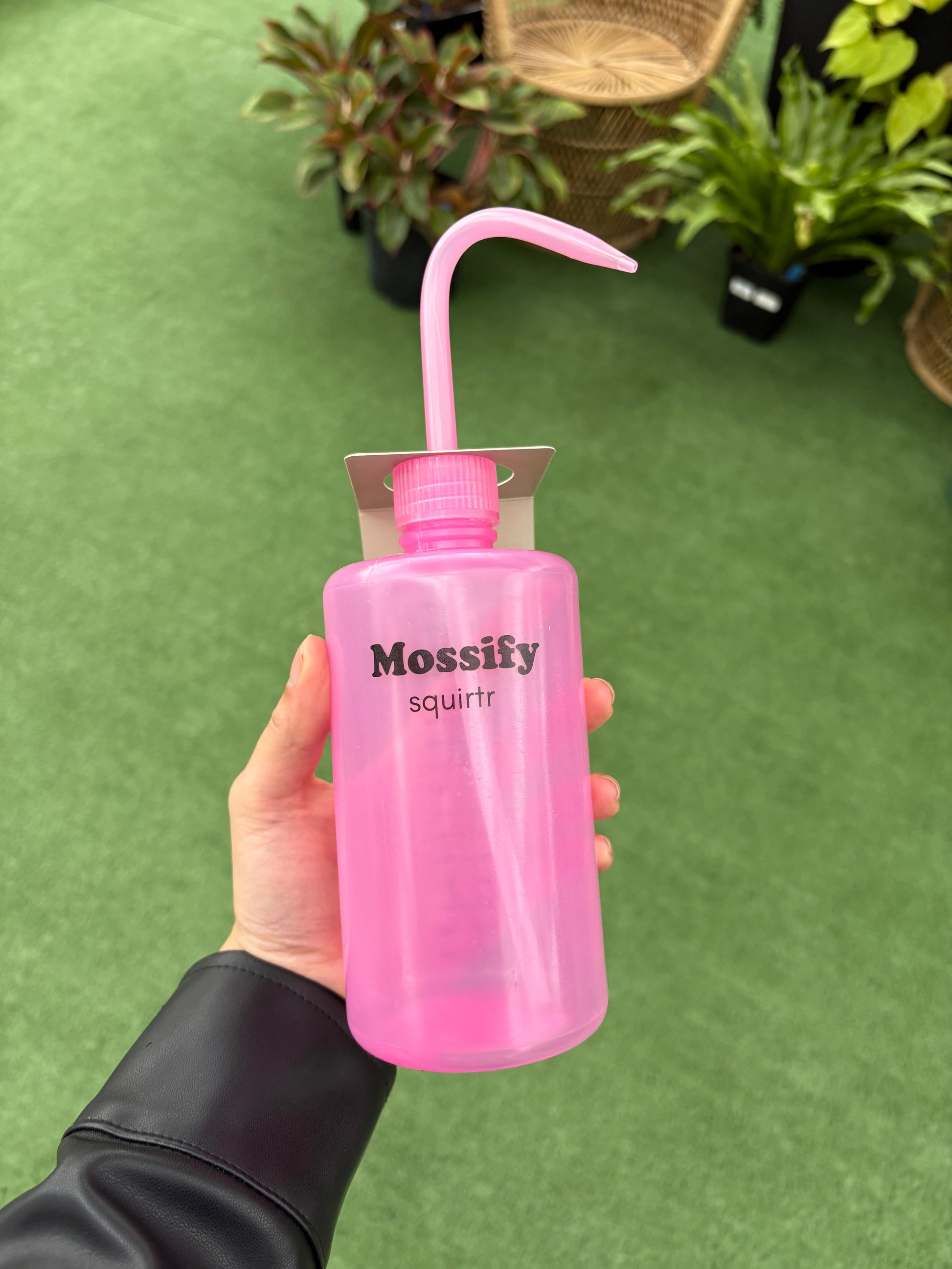 Pink 'Mossify' water bottle with a spout held by a hand on a green surface.