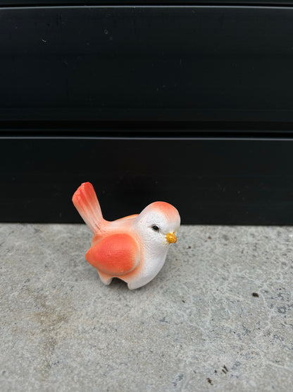 a ceramic orange and white bird resting on a concrete surface