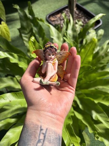 Hand holding a small fairy figurine with green leaves in the background