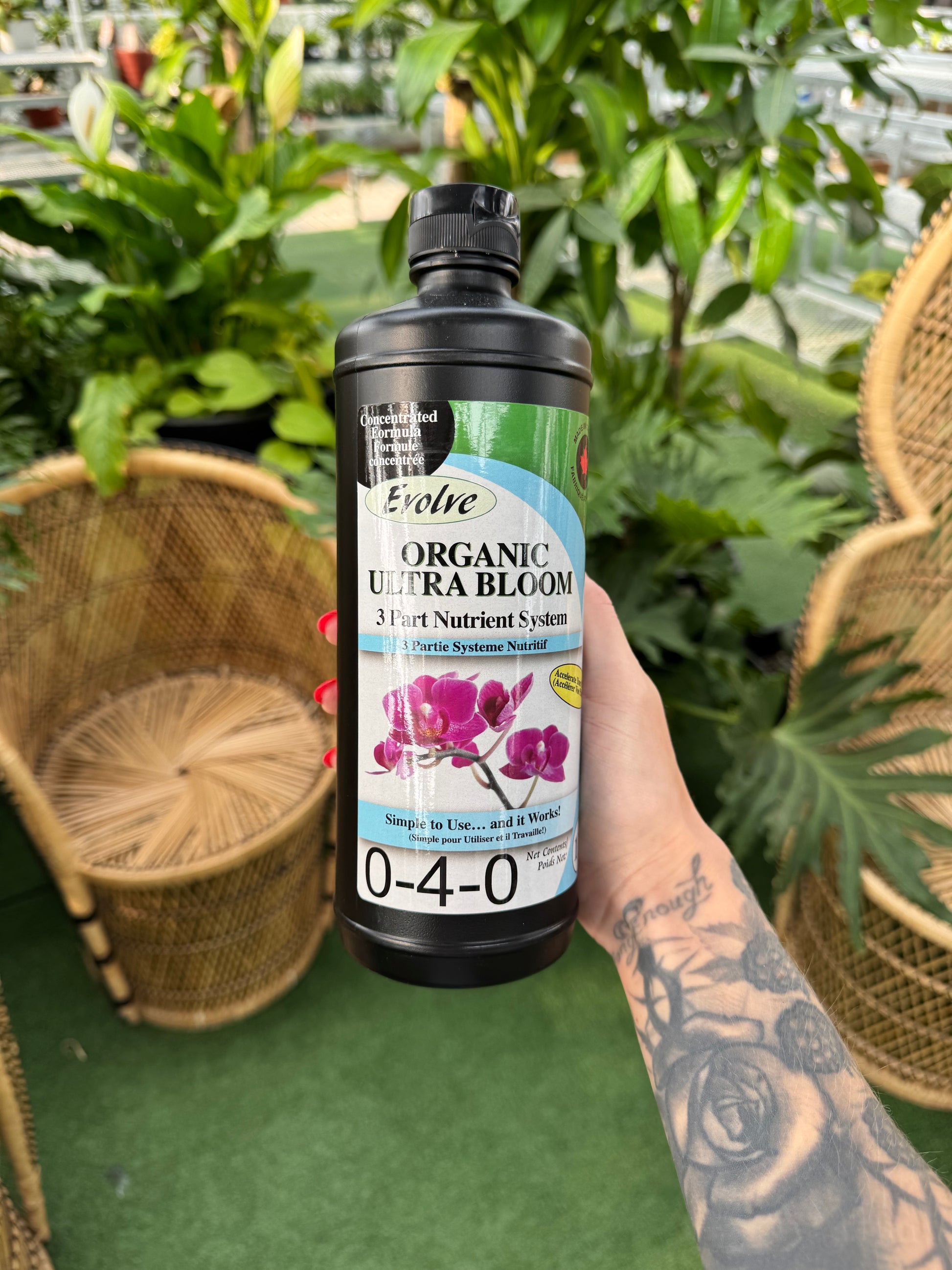 Hand holding a bottle of evolve Organic Ultra Bloom fertilizer with plants in the background