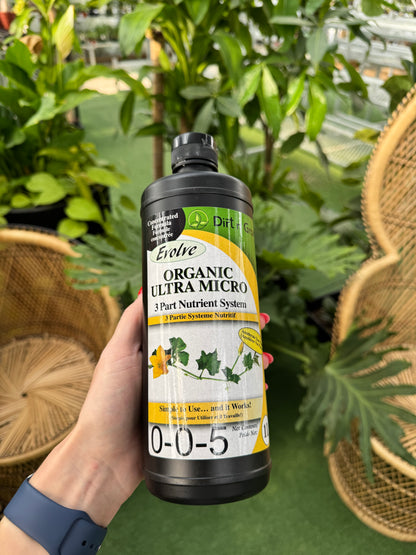 hand holding a bottle of evolve organic ultra micro plant fertilizer in a greenhouse setting