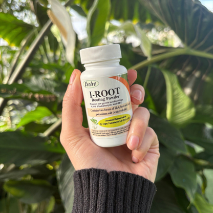 a person holding a small white bottle labeled I-ROOT rooting powder with plants in the background
