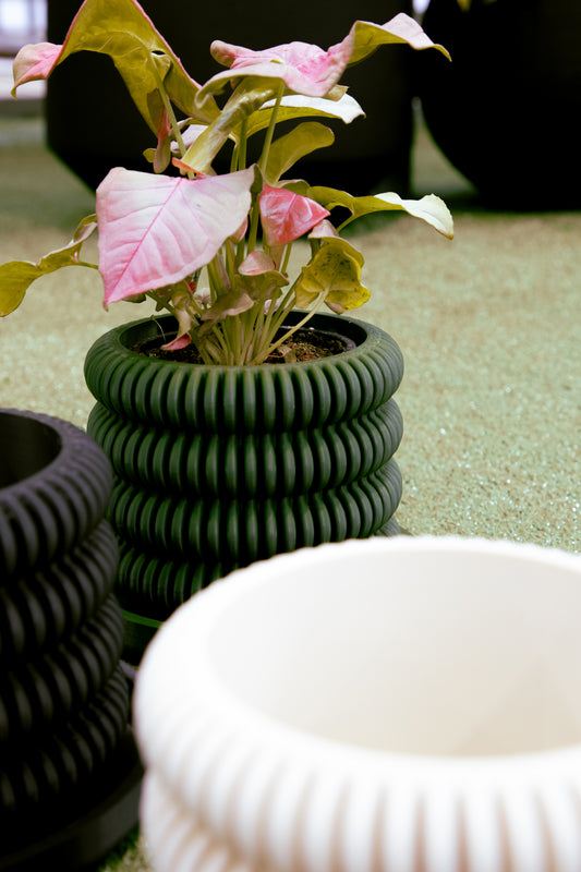 A green, pagoda-inspired ceramic pot with a plant inside, placed on a surface with other pots in the background.
