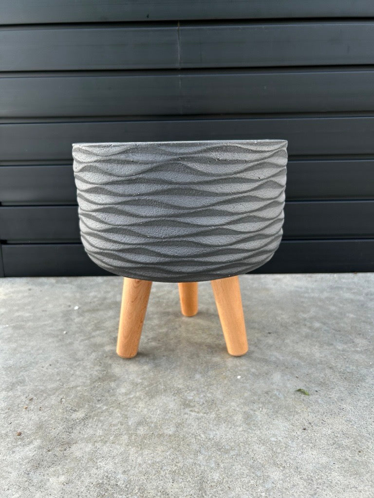 A round, matte black planter with a geometric pattern, displayed on a wooden leg, against a black background.