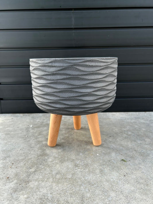 A round, matte black planter with a geometric pattern, displayed on a wooden leg, against a black background.