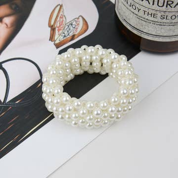 A white pearl scrunchie on a printed text background.