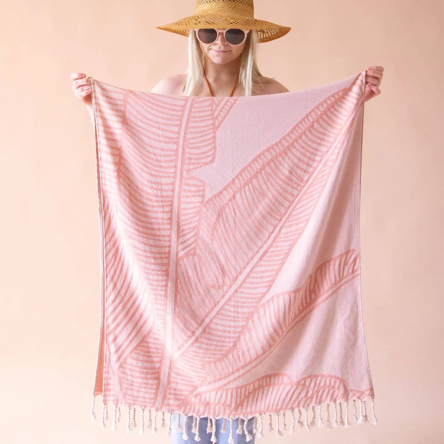 a person holding up a pink beach towel with a leaf pattern