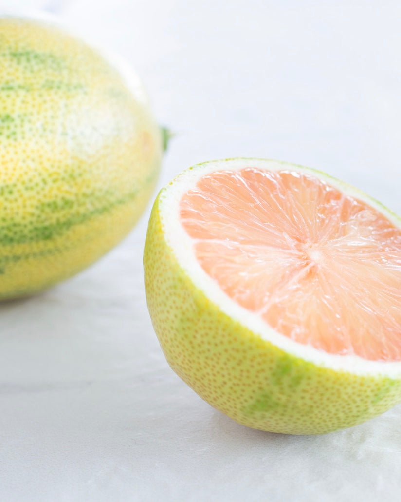 pink lemon citrus fruit with one half sliced open on a white background