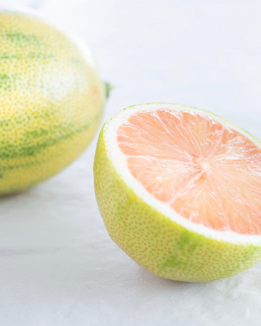 pink lemon citrus fruit with one half sliced open on a white background