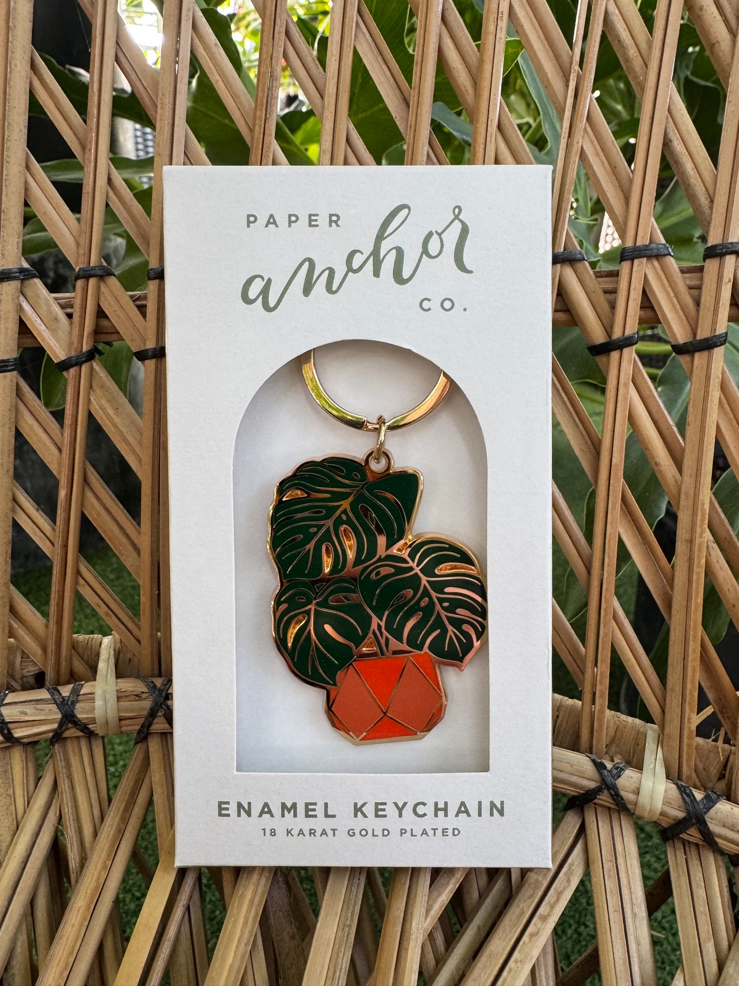 Enamel keychain with leaf design on a Paper Anchor Co. branded card, set against a woven background.
