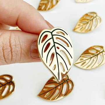 gold plant style pins held by a hand against a white background