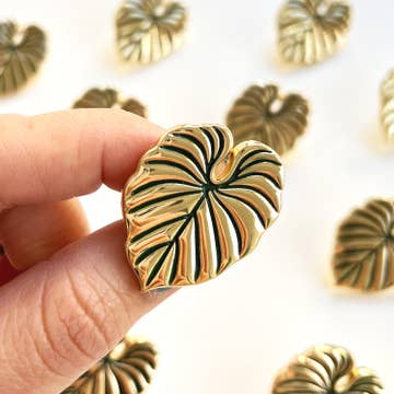 a collection of plant shaped gold pins held by a hand against a white background