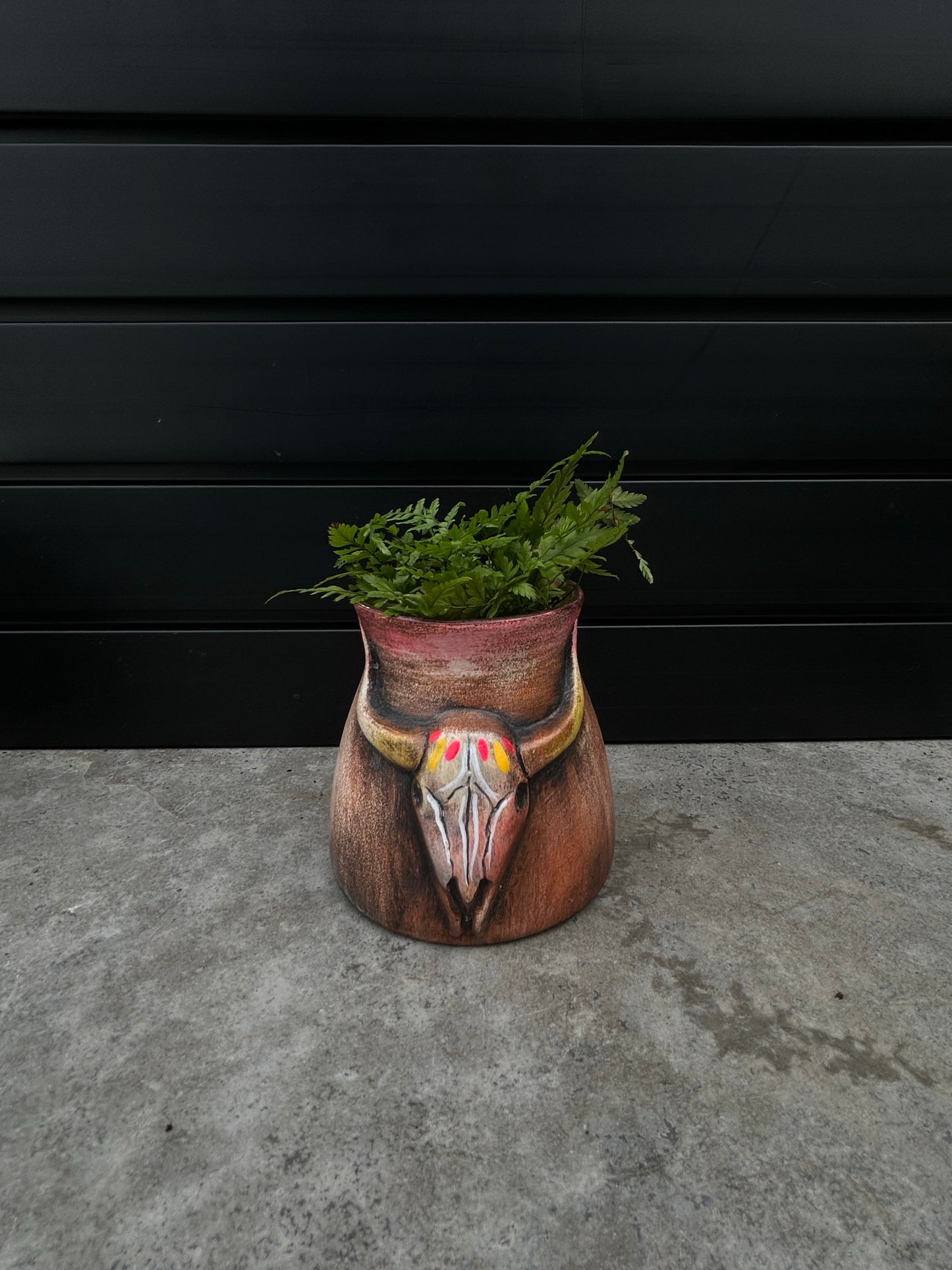a small brown ceramic planter with a bull skill design
