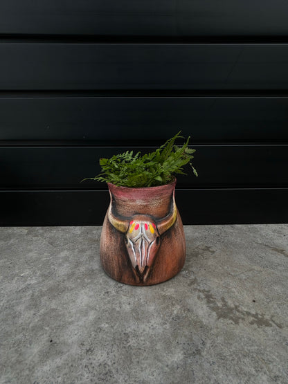 a small brown ceramic planter with a bull skill design