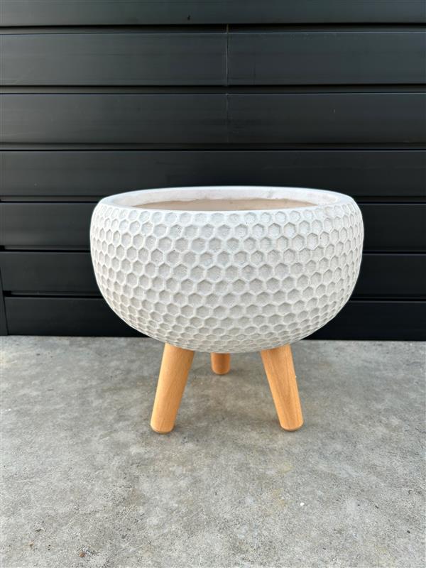 A white round honeycomb planter with wooden legs, placed against a black background.