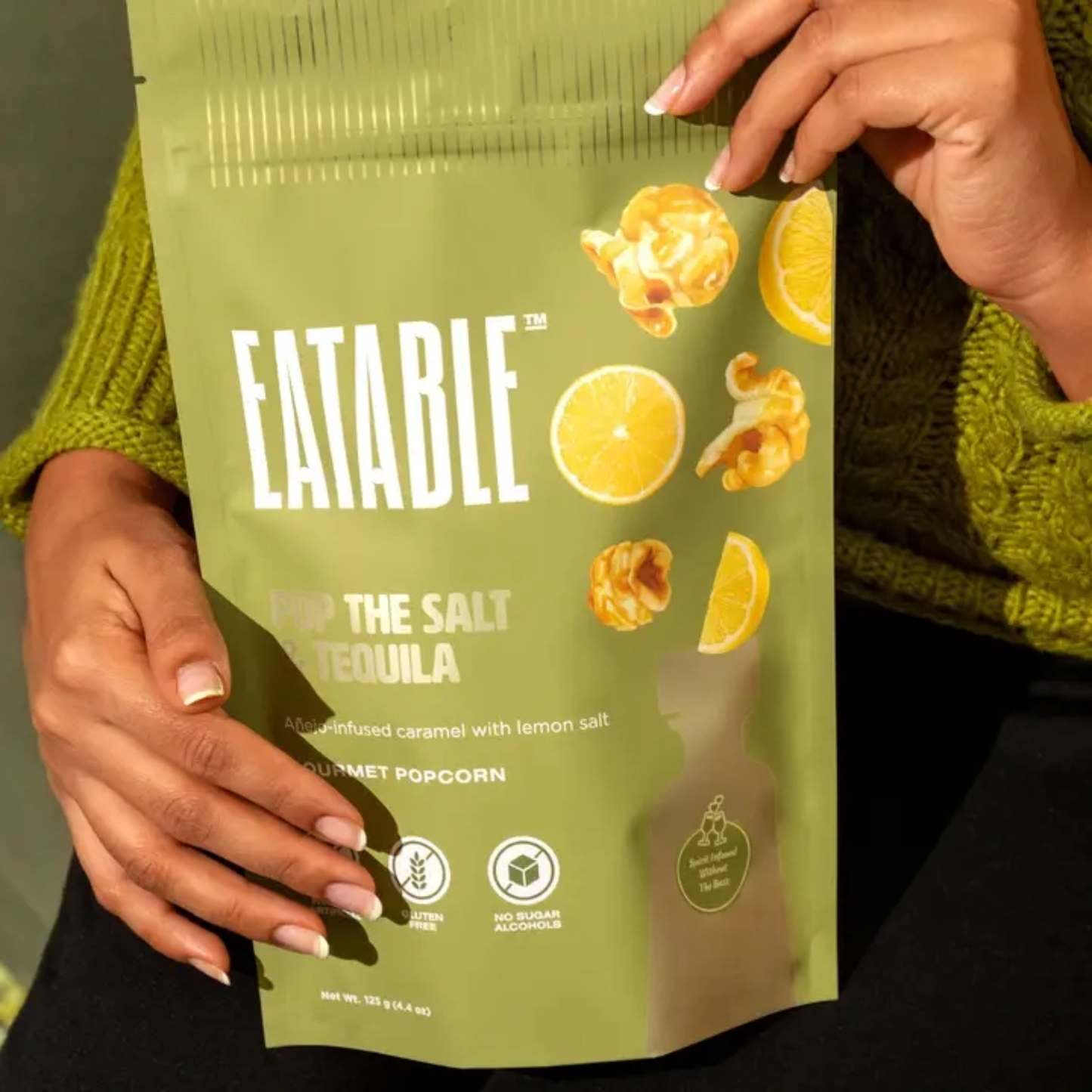 Green 'Eatable' popcorn bag with lemon salt and tequila flavor held by a person wearing a green sweater.