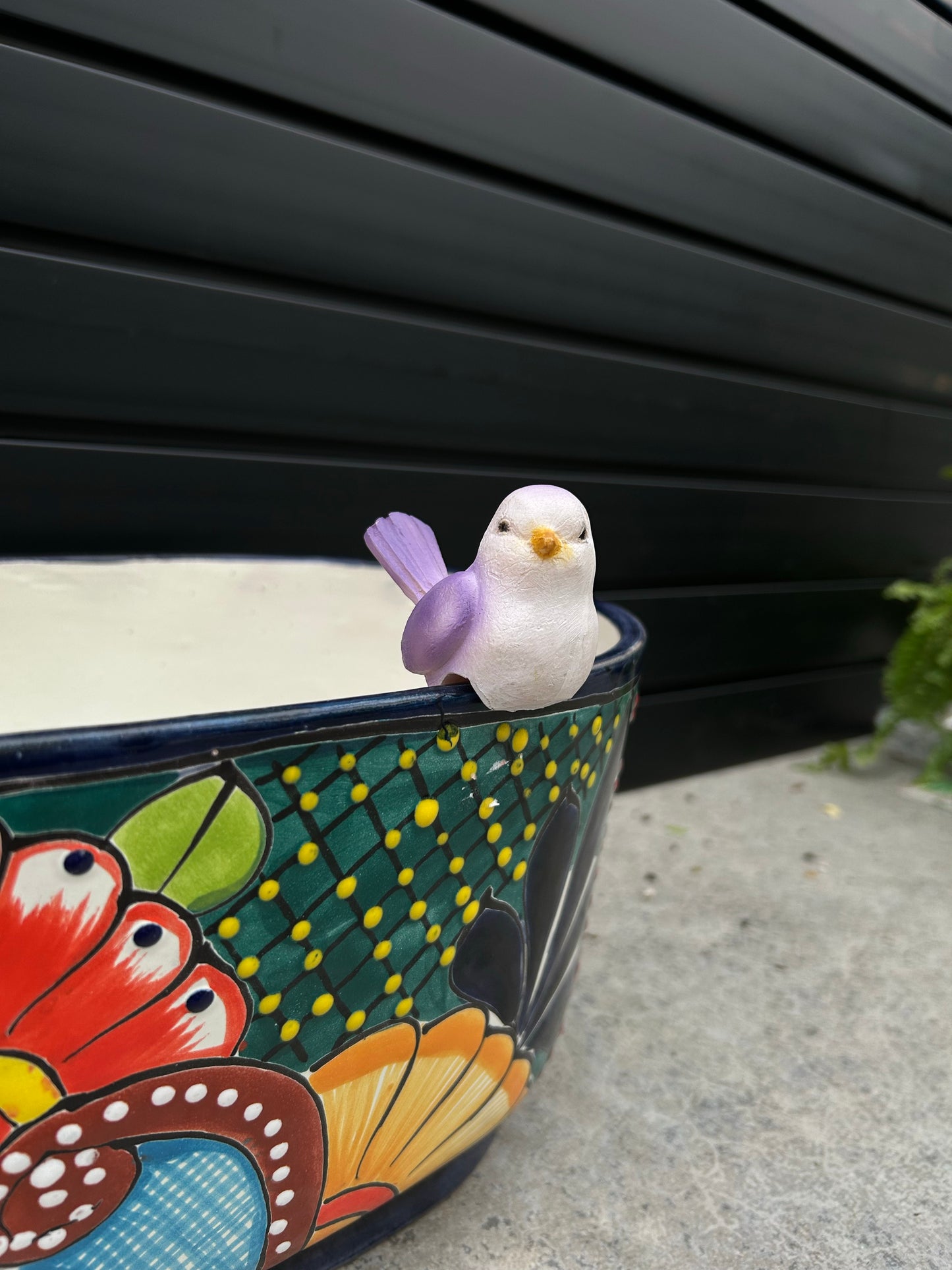 a small purple and white ceramic bird resting on a brightly coloured ceramic pot