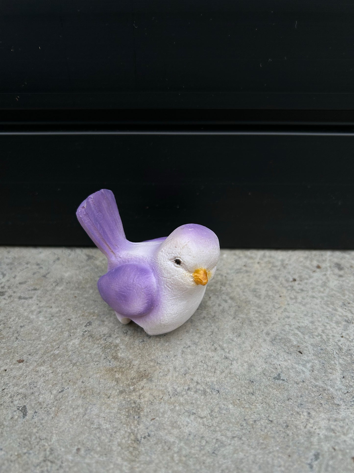 a ceramic purple and white bird resting on a concrete surface
