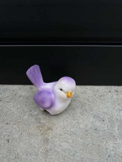 a ceramic purple and white bird resting on a concrete surface
