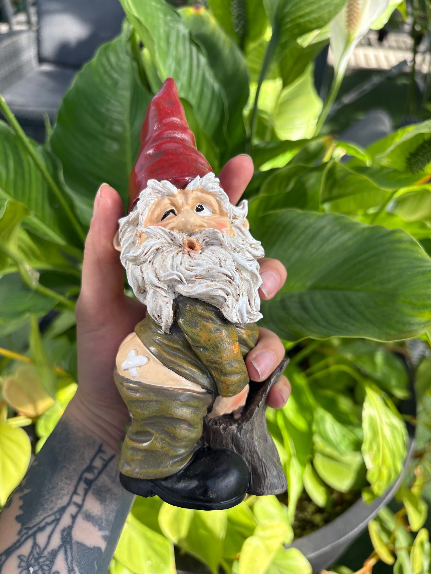 Hand holding a small gnome figurine with a blurred green plant background