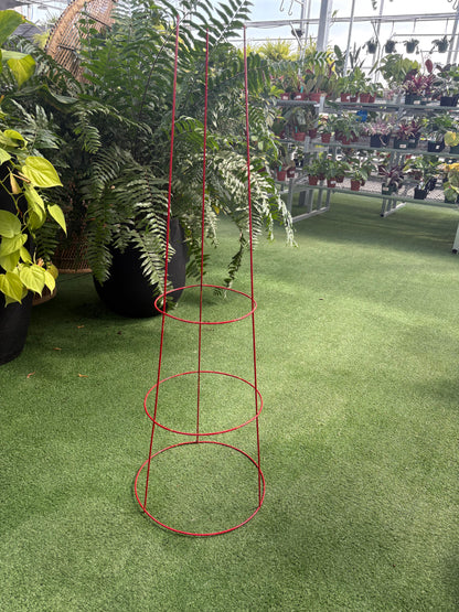 Red metal plant support cage on a green artificial grass surface with plants in the background.