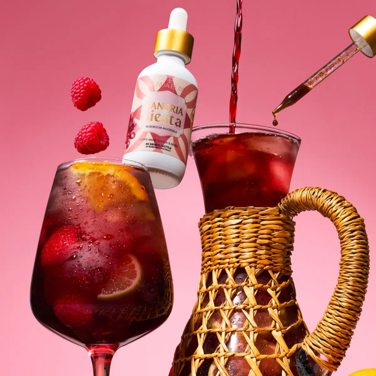 a small white bottle with a red label that reads sangria siesta mushroom mocktail resting between a sangria cocktail and a large pitcher of sangria with a pink background