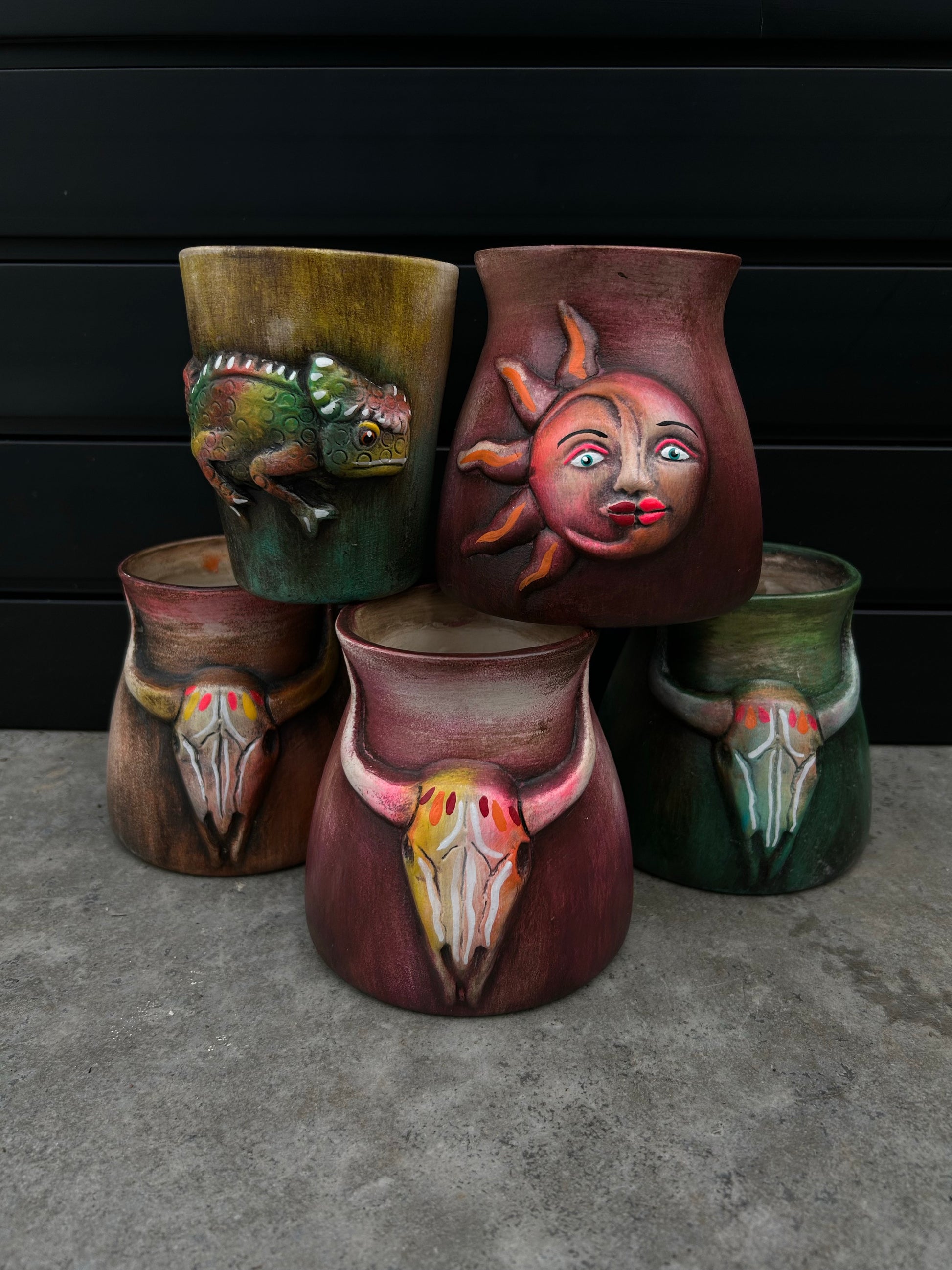stack of five pots wit varying designs including ram skulls, sun and moon, and chameleon