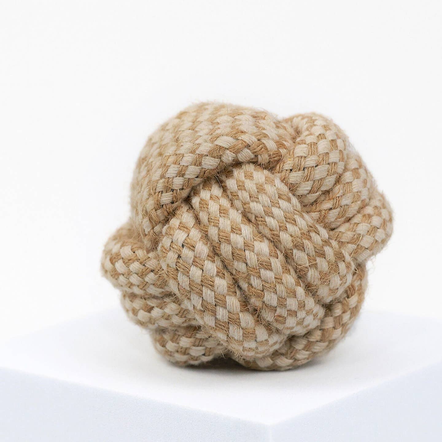 A small hemp rope dog toy, with a braided and twisted structure, primarily in a beige or light brown color.