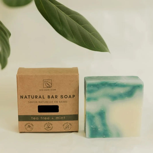 Two natural bar soaps with a swirled blue and white design, one placed in front of the other, beside a cardboard packaging labeled 'Natural Bar Soap, Tea Tree & Mint'.