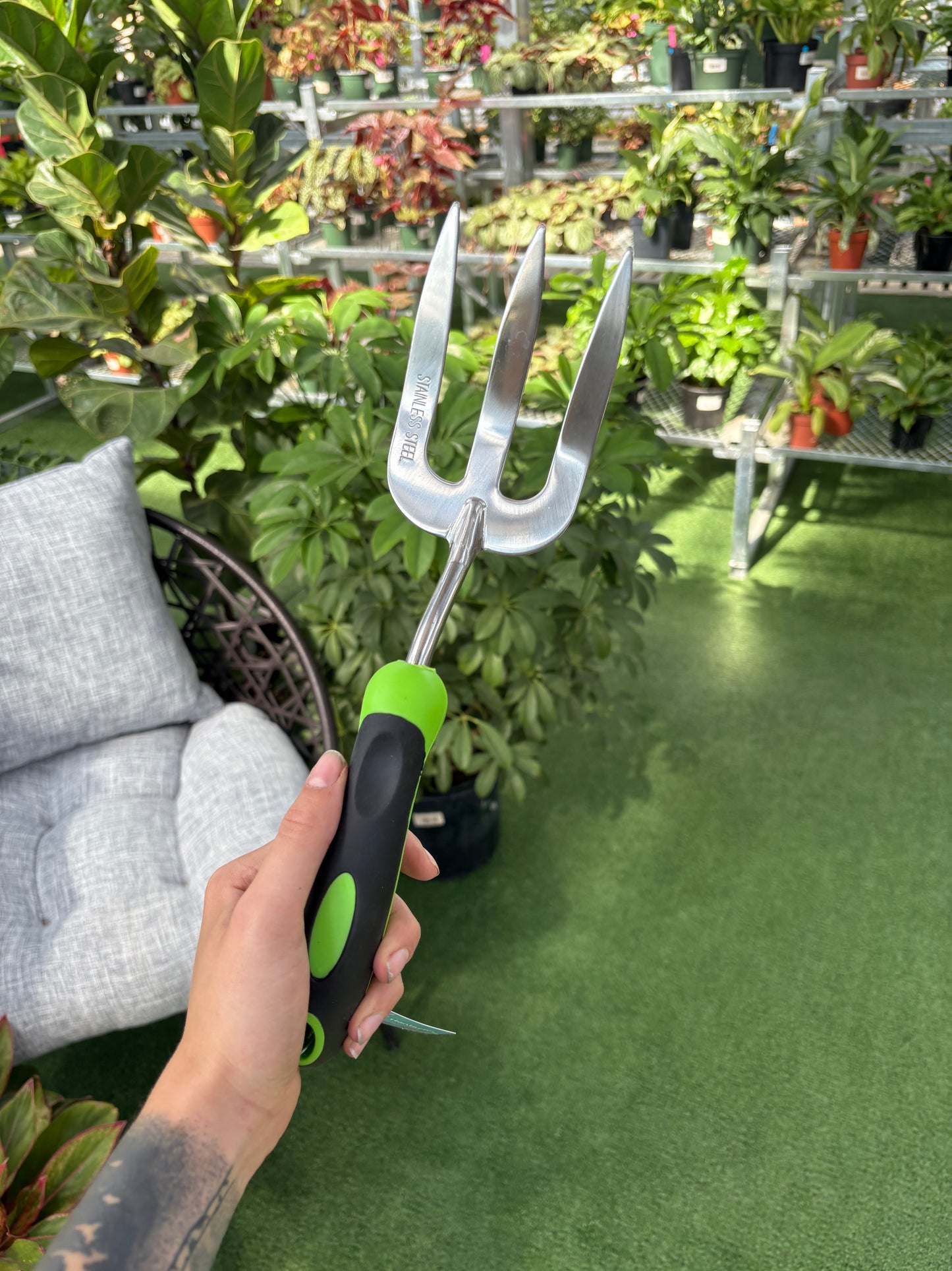 Person holding a garden tool with a green handle in front of plants