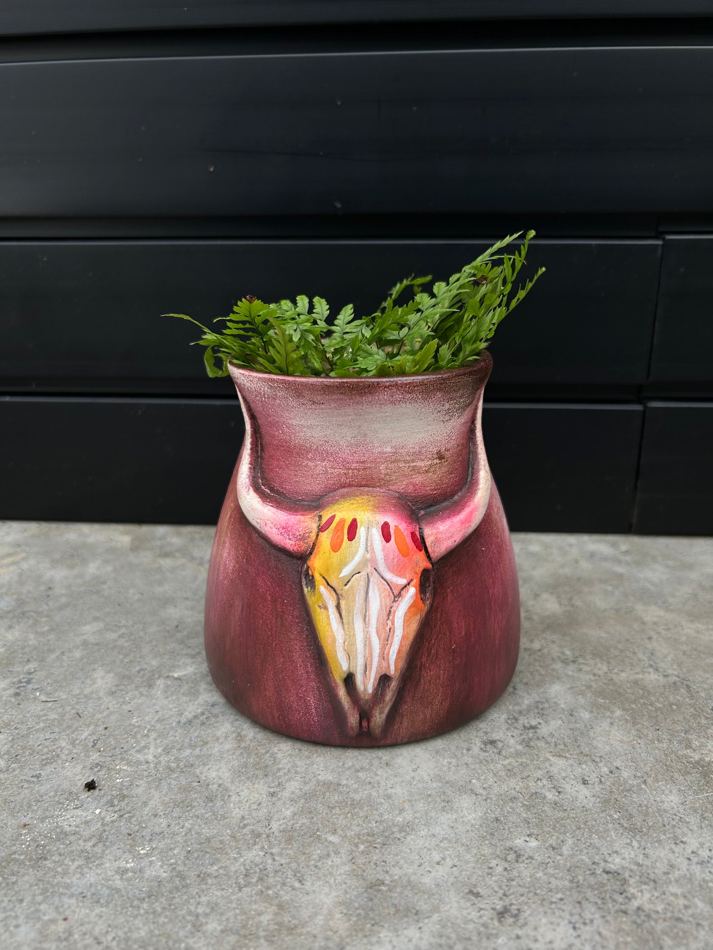 a small ceramic red pot with a bull skull design