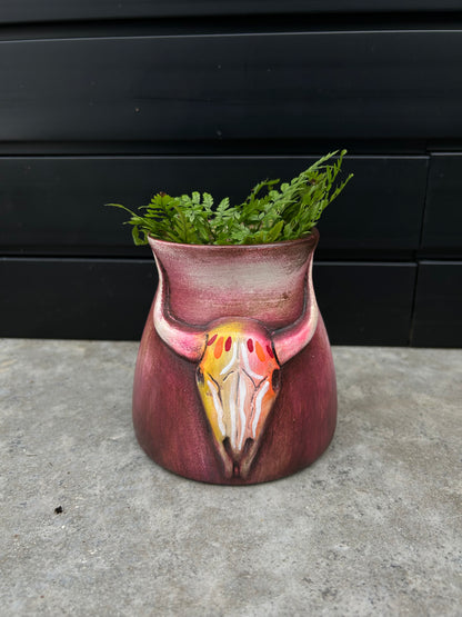 a small ceramic red pot with a bull skull design