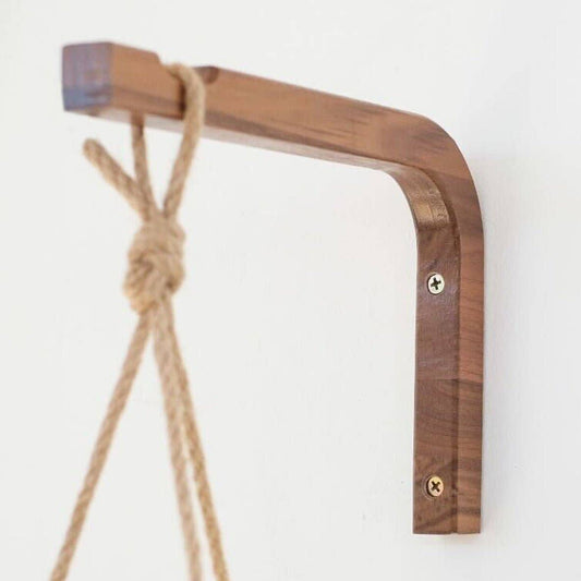 A walnut and birch wood wall hanger with visible wood grains, attached to a wall mount, supporting a hanging plant.