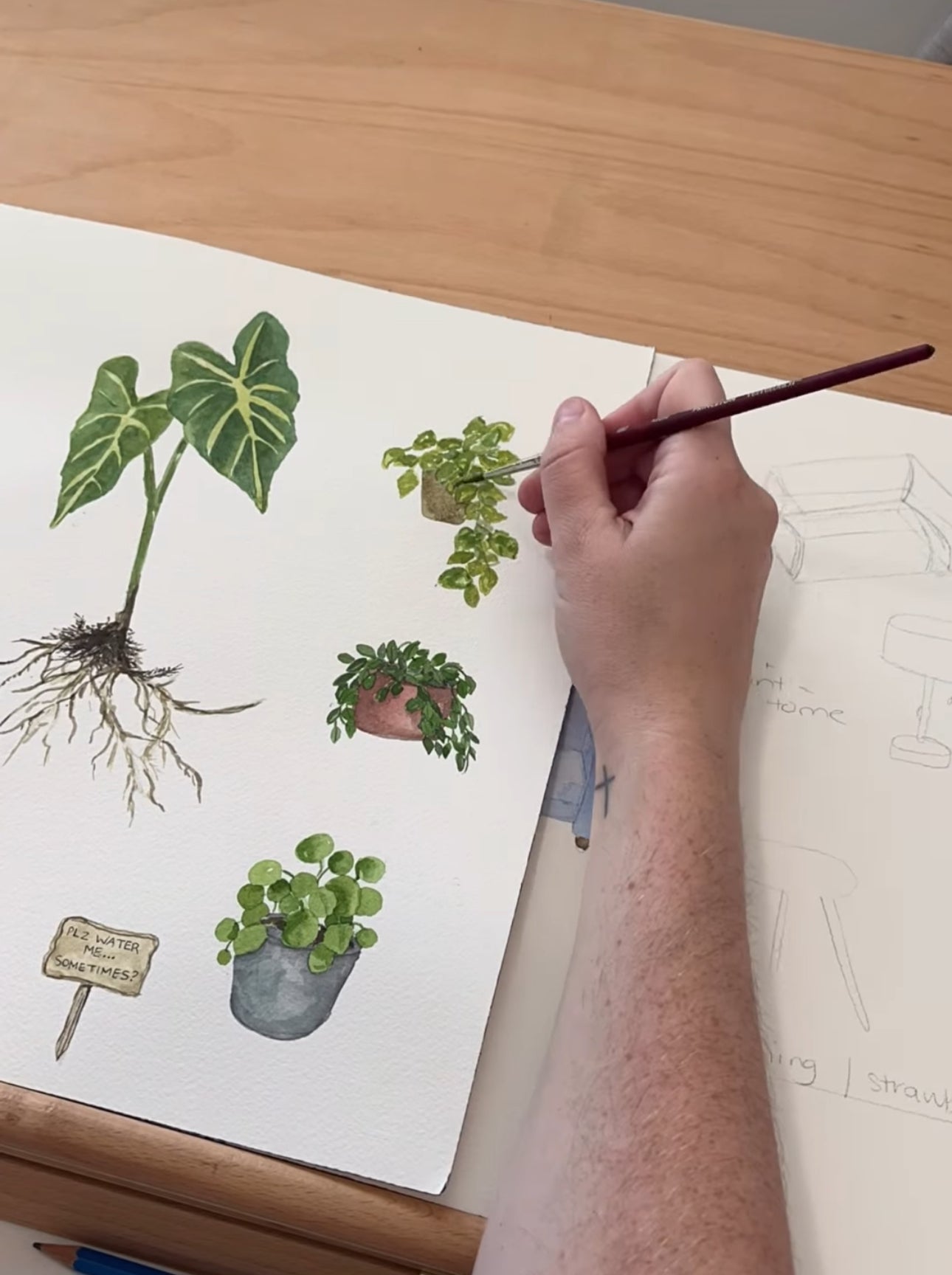 Hand painting watercolour plants on a piece of paper with a wooden surface underneath