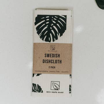 A pack of two white dishcloths with a black leaf pattern, labeled 'SWEDISH DISHCLOTH' and branding information.